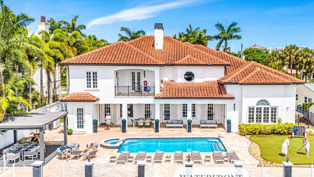A large white house with a red-tiled roof, a swimming pool, and a covered patio area.