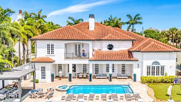 Uma casa grande e branca com telhado de telhas vermelhas, piscina e um alpendre coberto.
