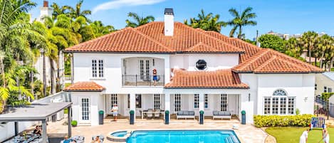A large white house with a red-tiled roof, a swimming pool, and a covered patio area.
