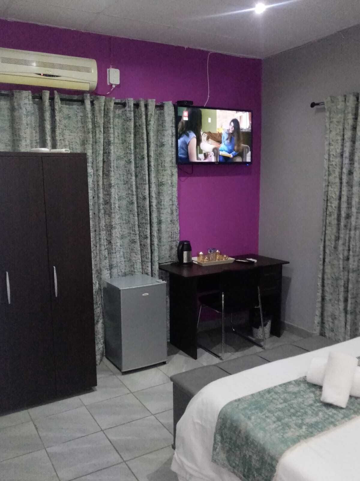 Une chambre avec un lit, un bureau, un petit réfrigérateur et un téléviseur fixé au mur.