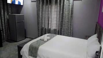 A hotel room with a bed, a TV mounted on the wall, a small table, and a wardrobe.