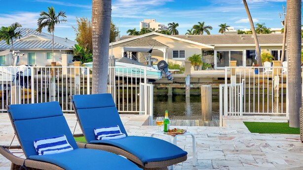 A poolside area with lounge chairs, a small table with a bottle and snacks, and a boat docked in the background. - Riviera Oasis: Waterfront, Pool, 5min To Beach (Fort Lauderdale)