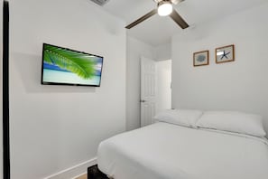 Une chambre à coucher avec un lit, un ventilateur de plafond, un téléviseur fixé au mur et deux tableaux encadrés.