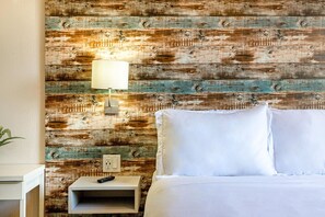 A hotel room with a rustic wooden wall, a bedside table with a lamp, and a bed with white linens.