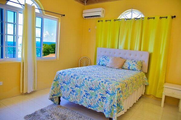Quarto com cama, janela com cortinas, ar condicionado e vista para o exterior.