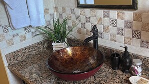 Baño con encimera de granito, lavamanos de pedestal, grifo negro, espejo y salpicadero de azulejos.