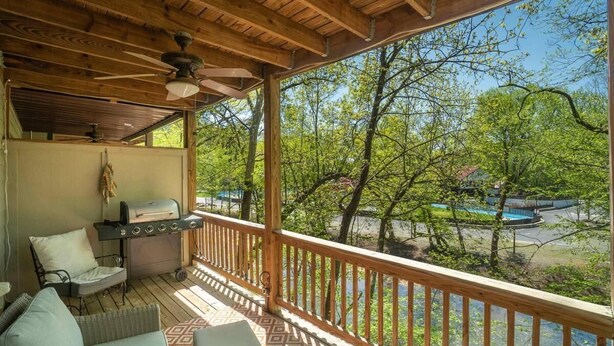 Un porche cubierto con una parrilla, muebles de exterior y vistas a una piscina y árboles.