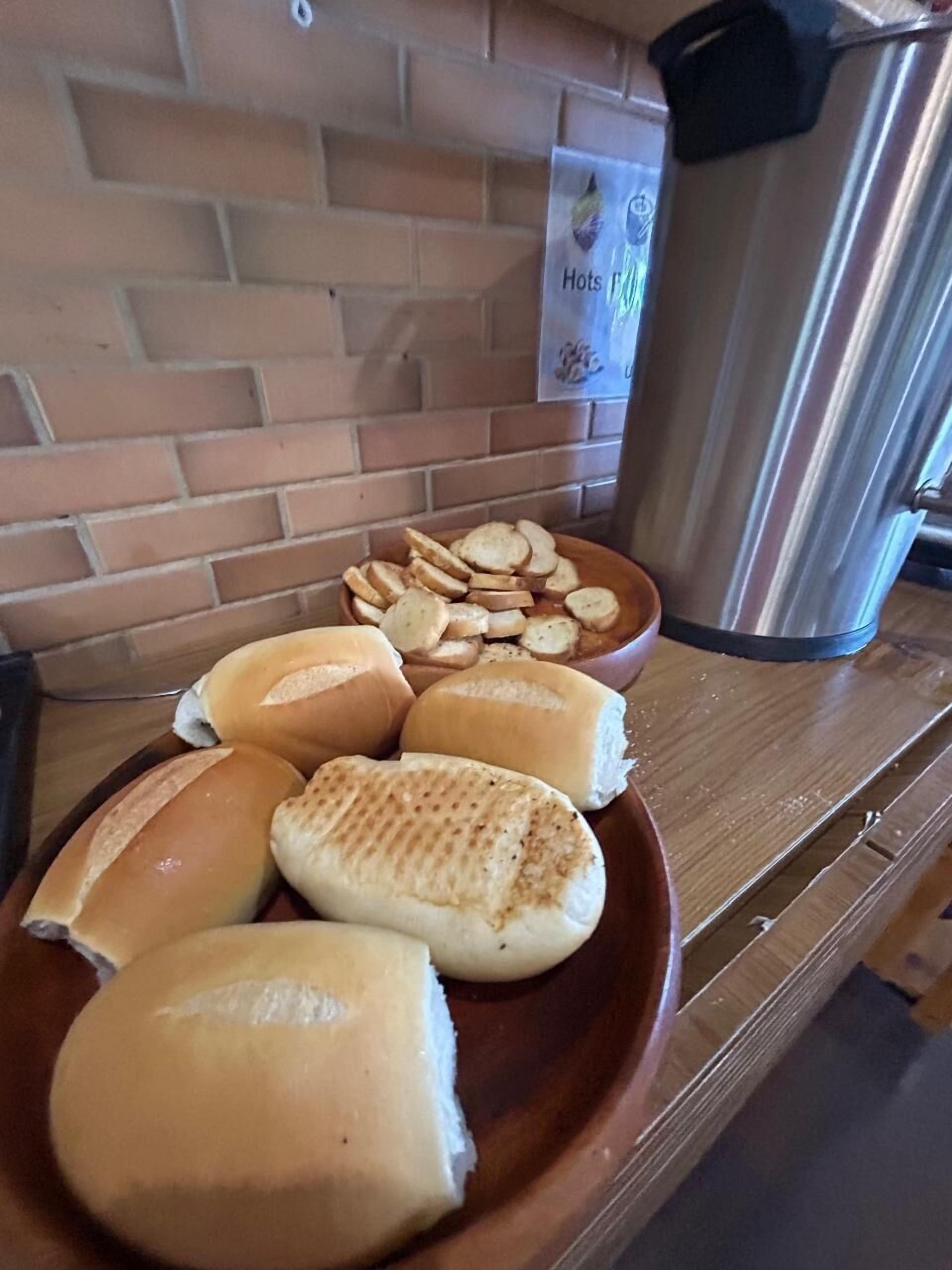 A plate with various bread items and a stainless steel kettle on a wooden table.