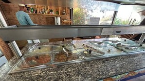 Een buffetgedeelte met verschillende glazen containers vol eten, een granieten aanrecht en uitzicht op de omgeving door een raam.
