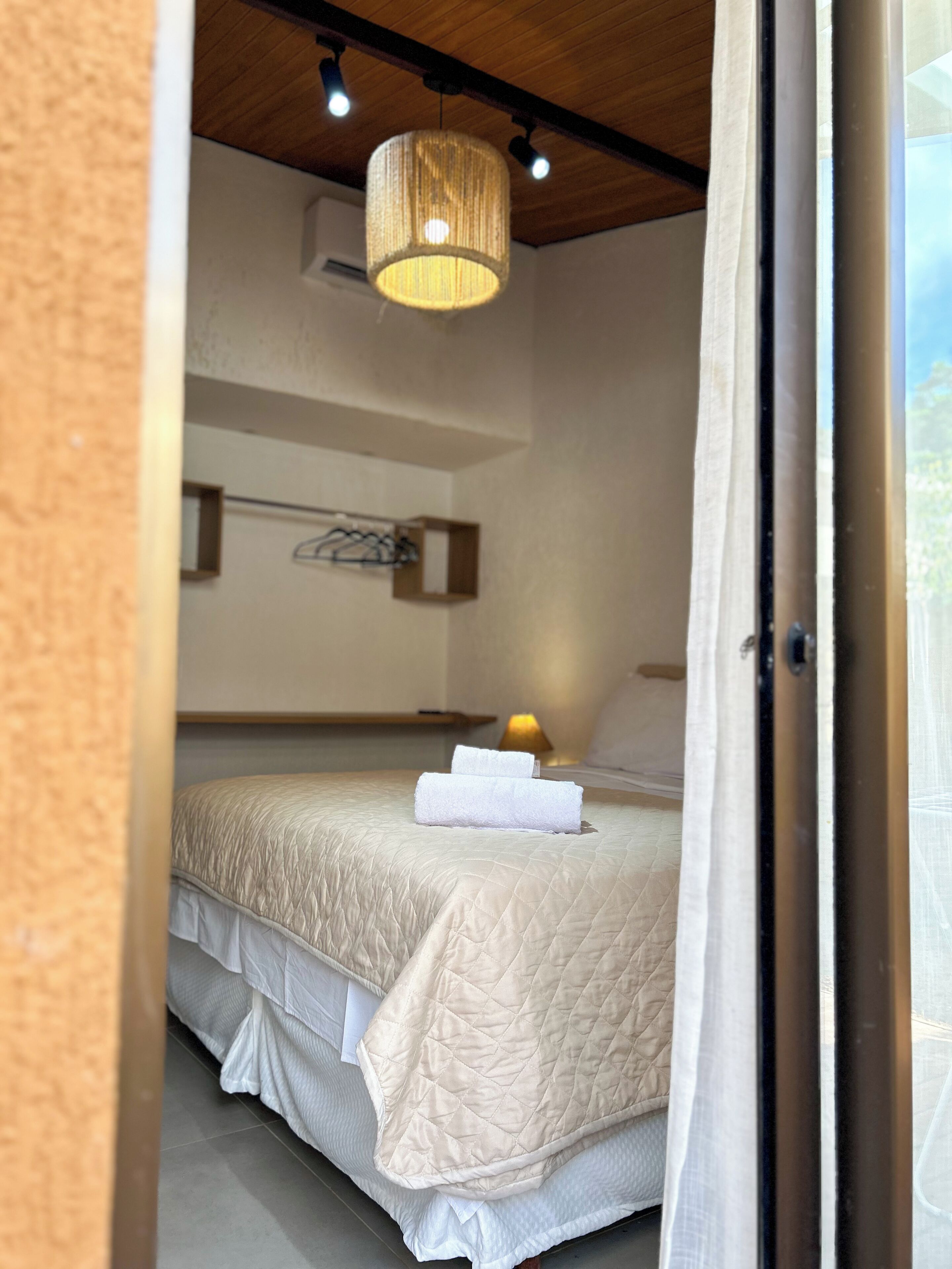 A bedroom with a bed, a hanging light fixture, and a view through an open door.