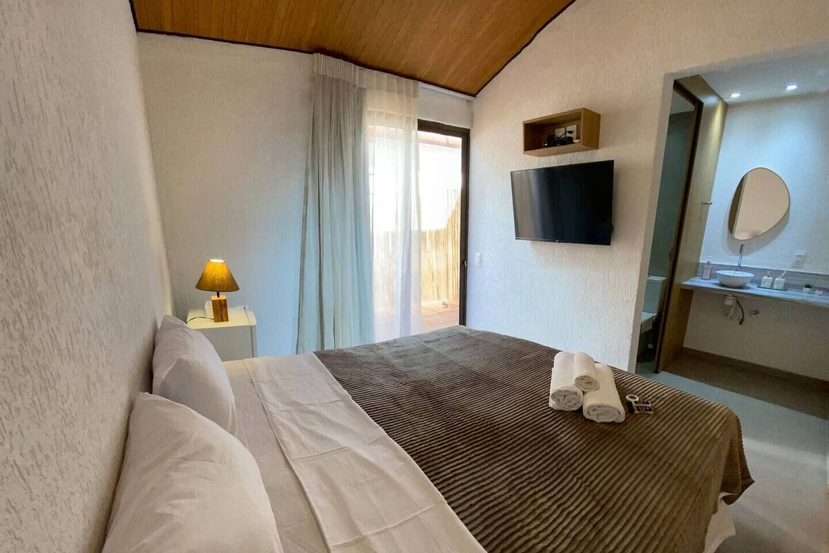 A bedroom with a bed, pillows, a bedside lamp, a TV, and a bathroom with a mirror and sink.