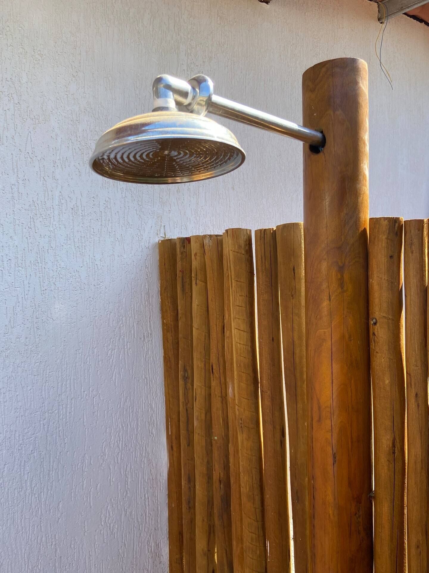 Une pomme de douche en métal fixée à un poteau en bois, le tout monté sur un mur blanc.