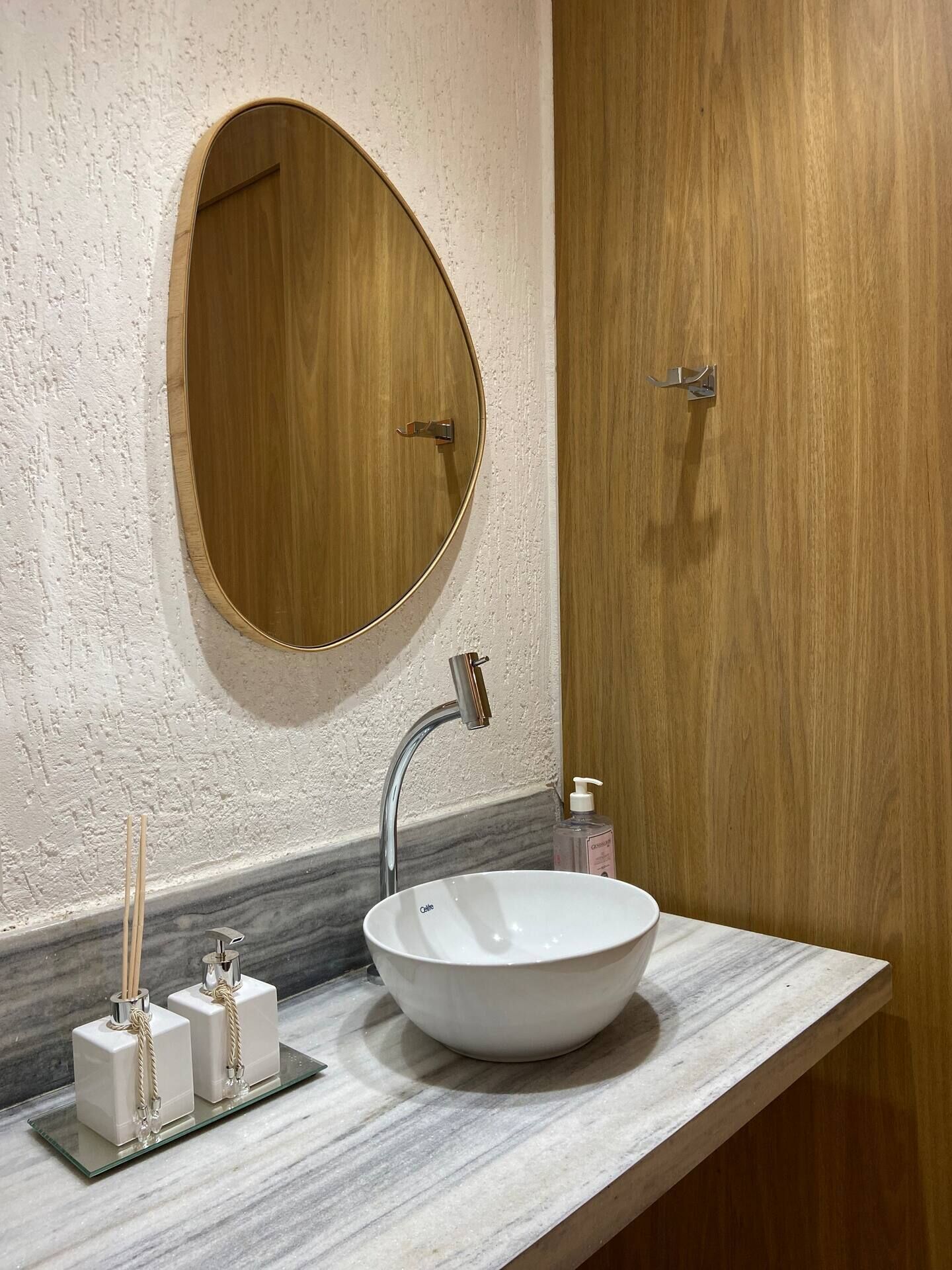 Een badkamer met een ronde spiegel, een wit wastafelmeubel en een houten deur.