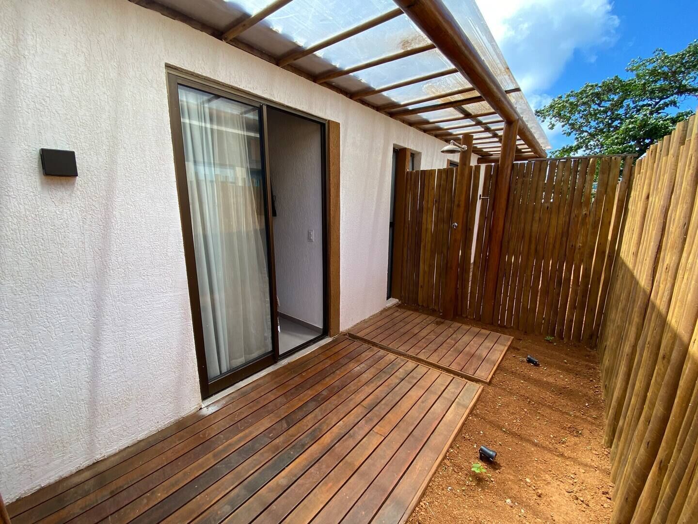Un'area patio coperta con un pavimento in legno, una porta scorrevole in vetro e una recinzione di legno.