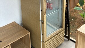 Een houten koelkast met glazen deur, voorzien van het label 'Corona', met flessen en blikjes.