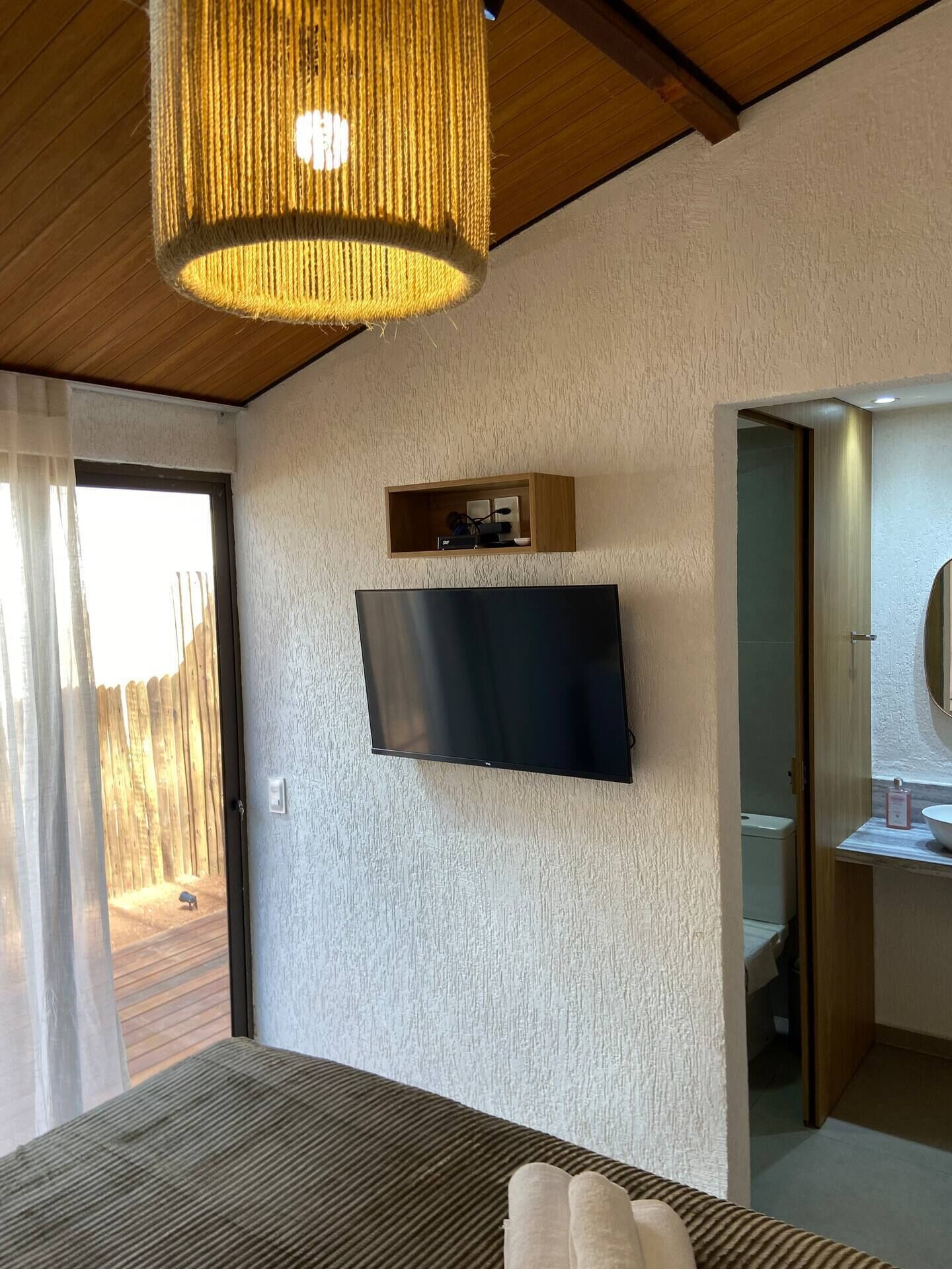 Une chambre à coucher avec un lit, un téléviseur fixé au mur, un plafond en bois et une porte donnant sur un balcon.