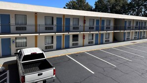 Un motel con varias habitaciones, un estacionamiento y una camioneta pickup blanca estacionada al frente.