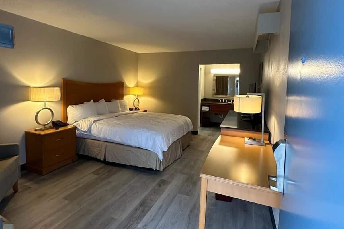 A hotel room with a bed, bedside tables, a desk, and a mirror.