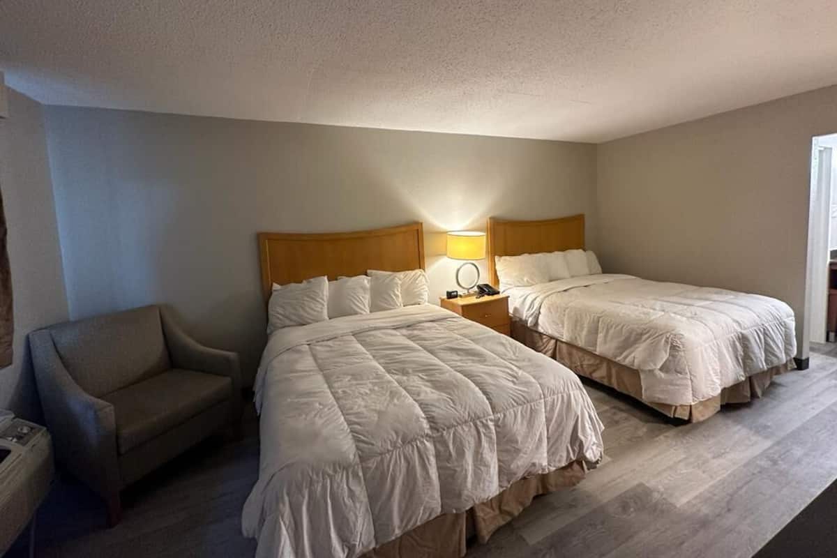 A hotel room with two beds, a chair, a nightstand with a lamp, and a mirror.
