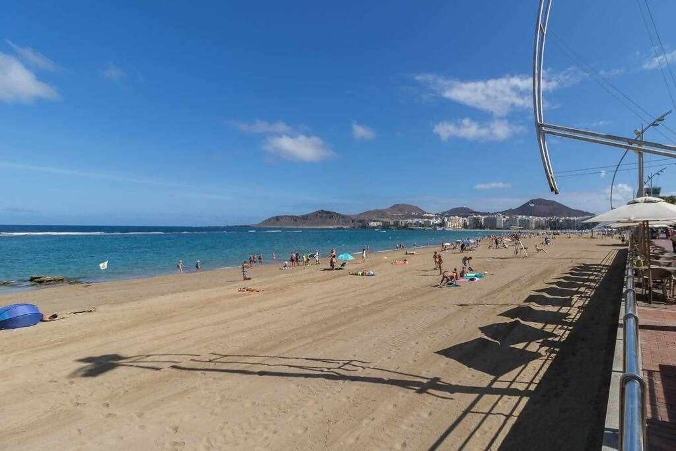 A beach with people, umbrellas, and a clear sky.