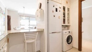 A compact kitchen with a built-in washing machine, a refrigerator, and a bar counter. - Oli Coral Canteras (Palmas De Gran Canaria, Las)