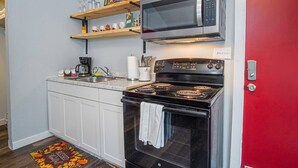 A compact kitchen with white cabinets, a black stove, a microwave, and a coffee maker. - Downtown Accessible New 1BR 1BA Cozy Studio (San Antonio)