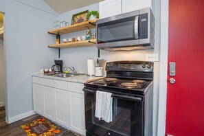 Uma cozinha compacta com armários brancos, um fogão preto, micro-ondas e cafeteira.