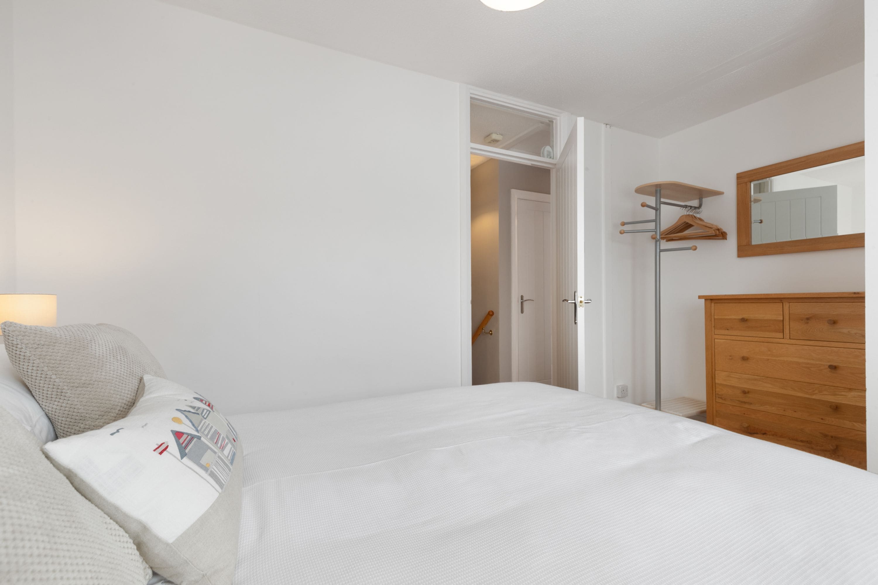 Une chambre à coucher avec un lit, une commode en bois, un miroir et une porte donnant sur une autre pièce.