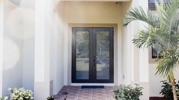 Un edificio moderno con doble puerta, vestíbulo con baldosas y plantas en macetas.