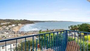 En balkon med udsigt over havet, en træstol og en flaske spiritus.