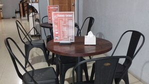 Ruokailutilassa on pyöreä pöytä ja kuusi mustaa tuolia. Pöydällä on esillä ruokalista, jonka otsikkona on ”Tummy Corner”.