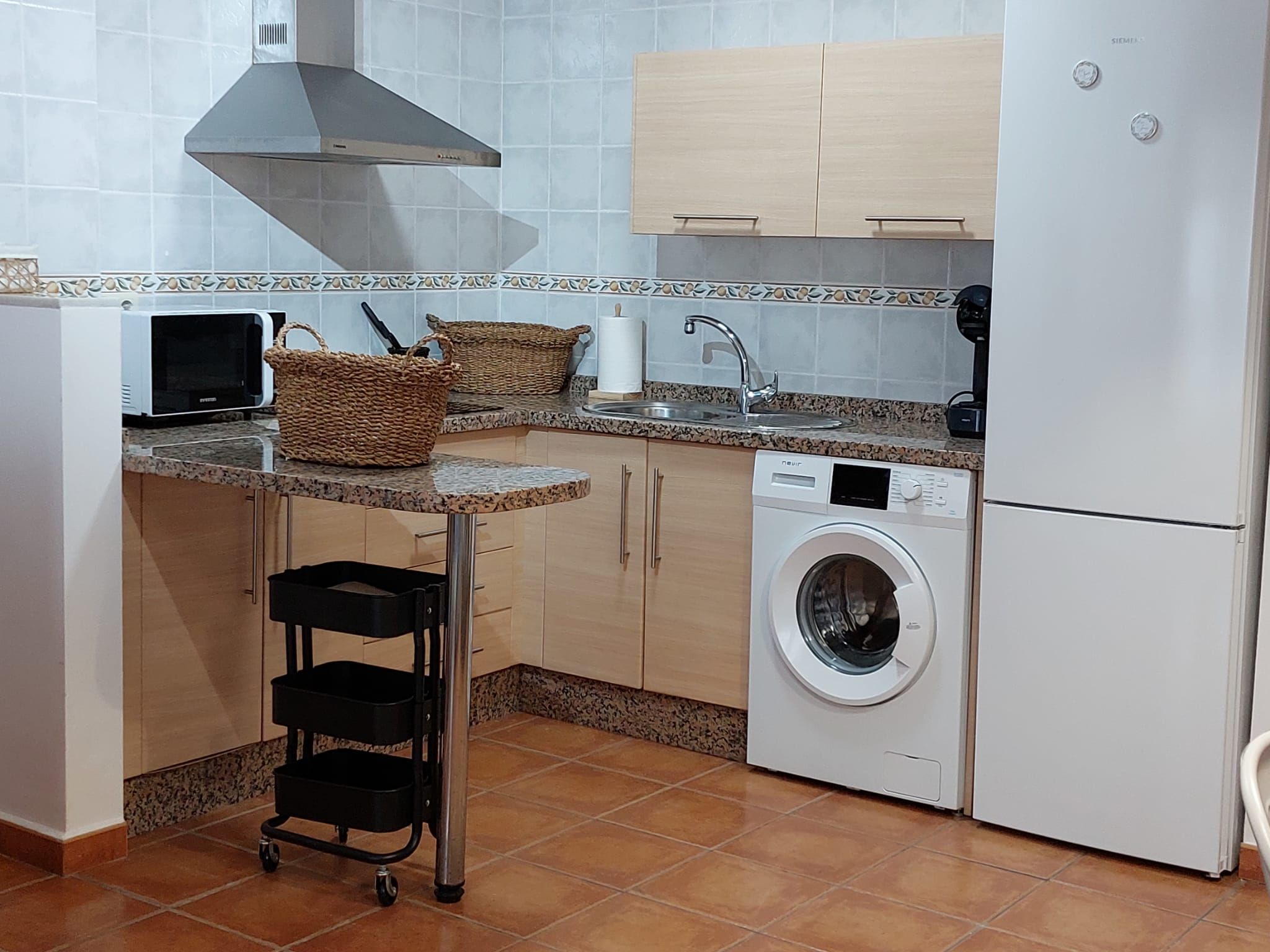 Une cuisine compacte équipée d’un lave-linge, d’un four à micro-ondes, d’un évier et d’une hotte aspirante.