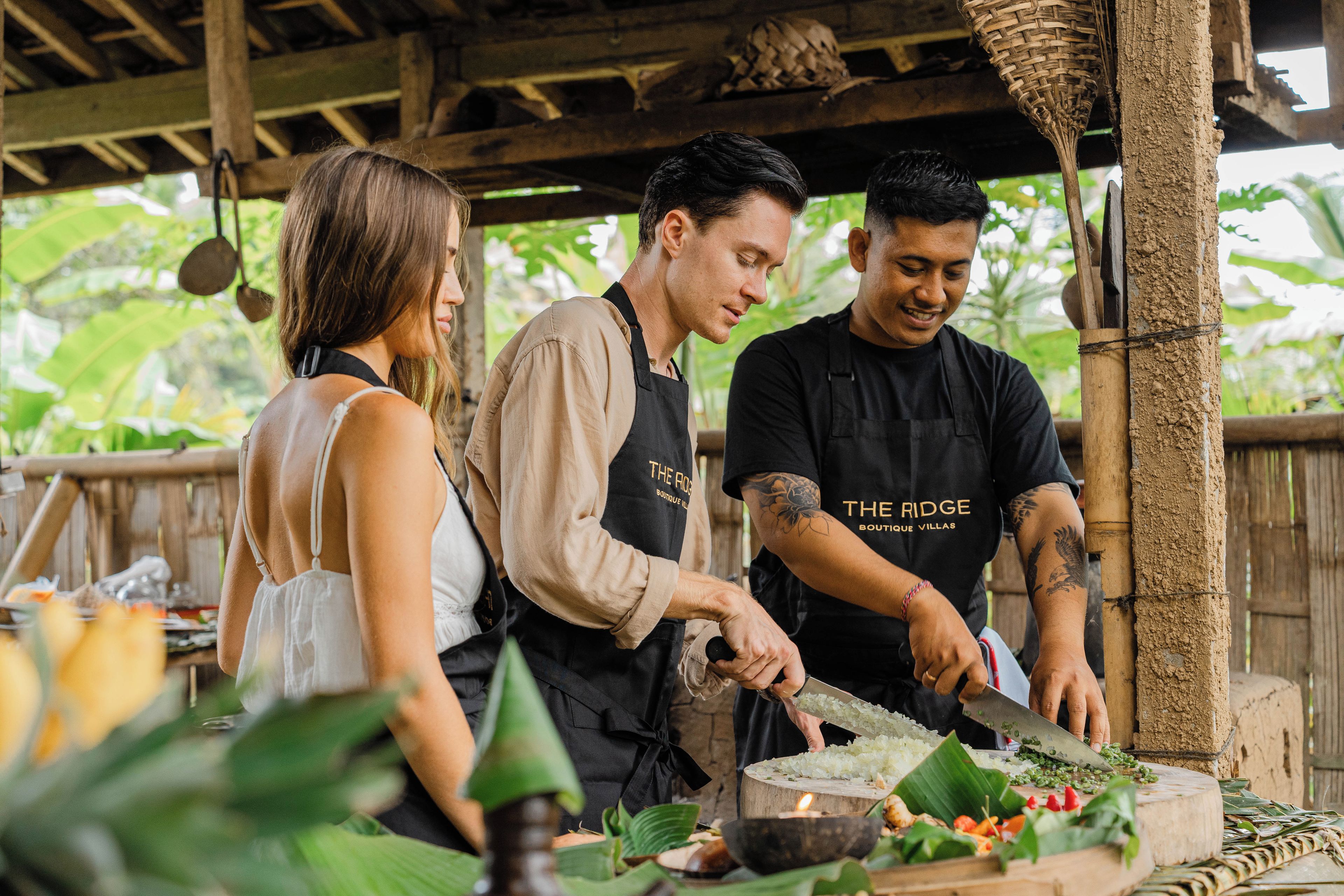 A group of people preparing food outdoors, with a rustic wooden structure and greenery in the background.