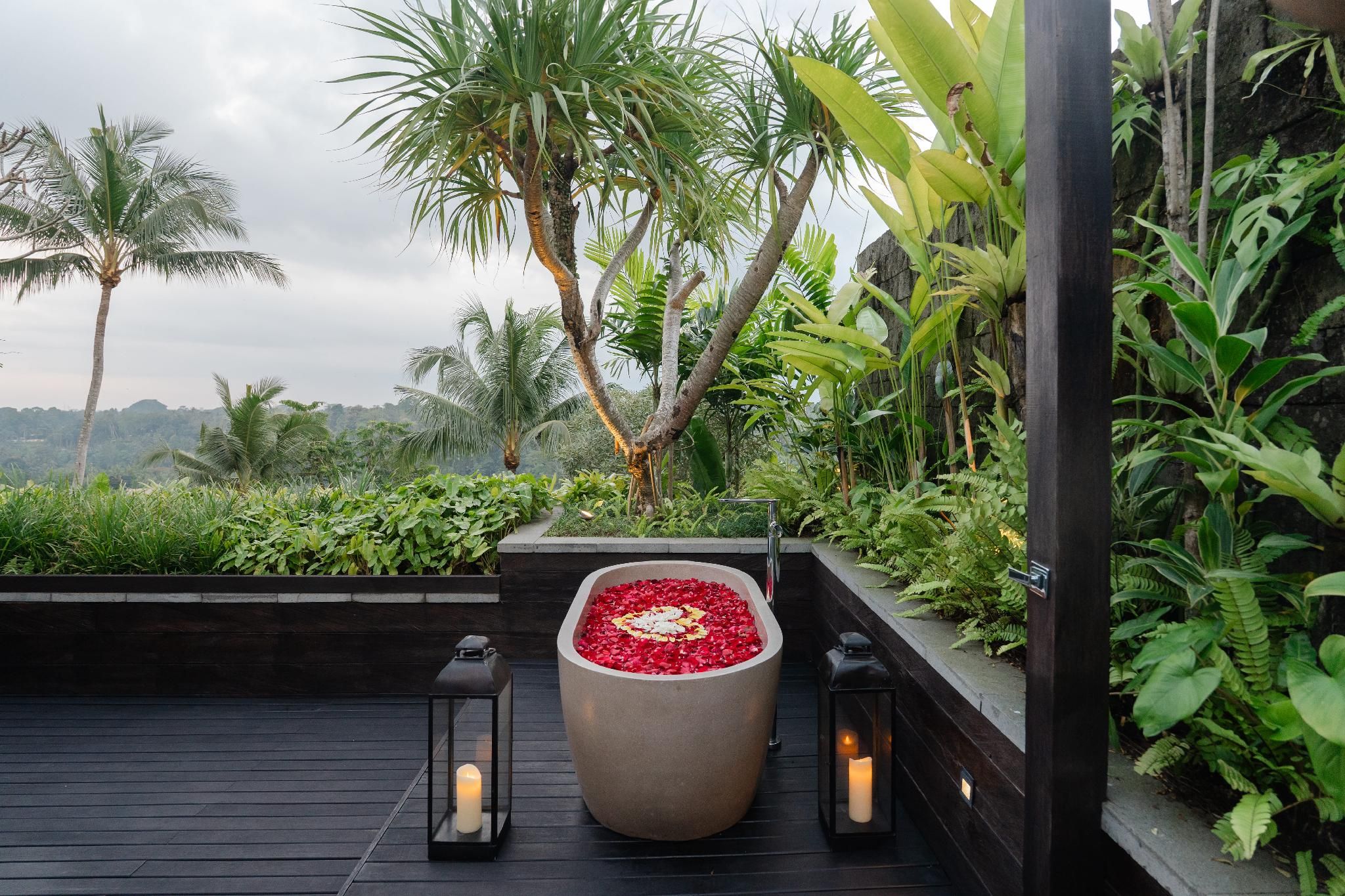 Un jardin sur le toit, avec un grand bac central rempli de fleurs rouges, entouré d’une végétation luxuriante et de palmiers.