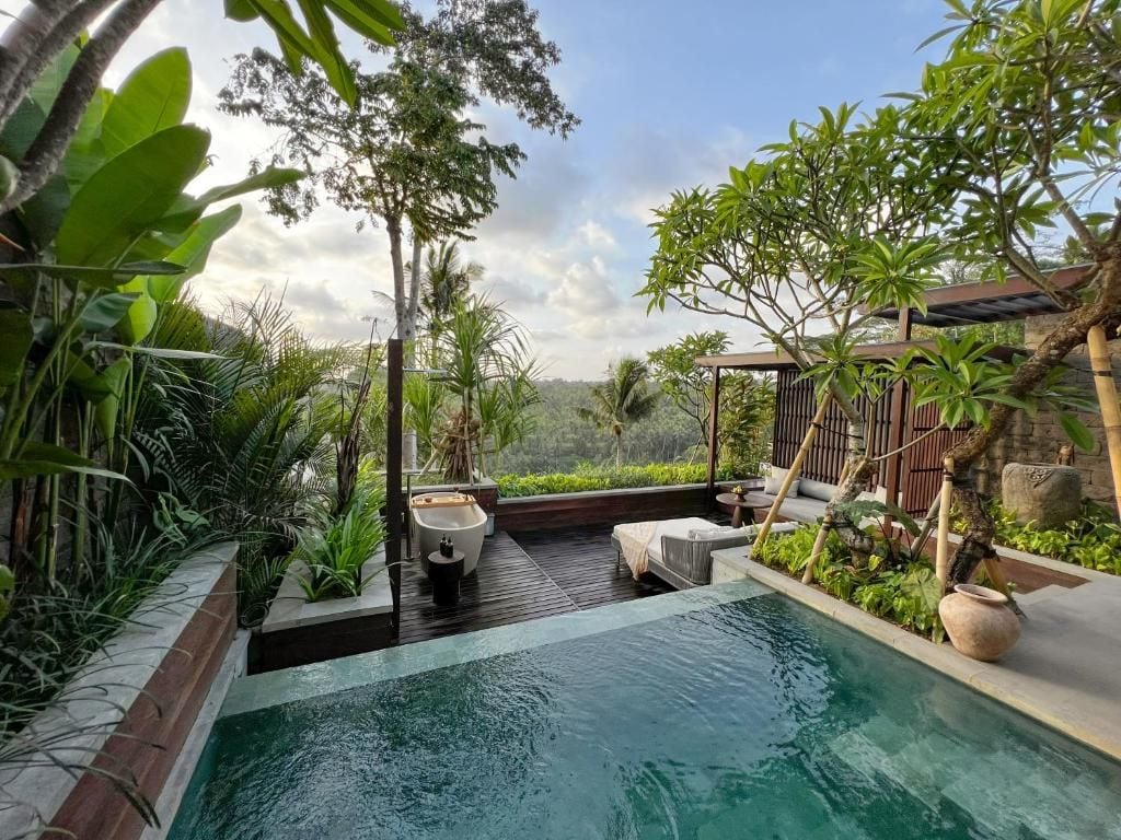 A pool area with a wooden deck, lounge chairs, and tropical plants.