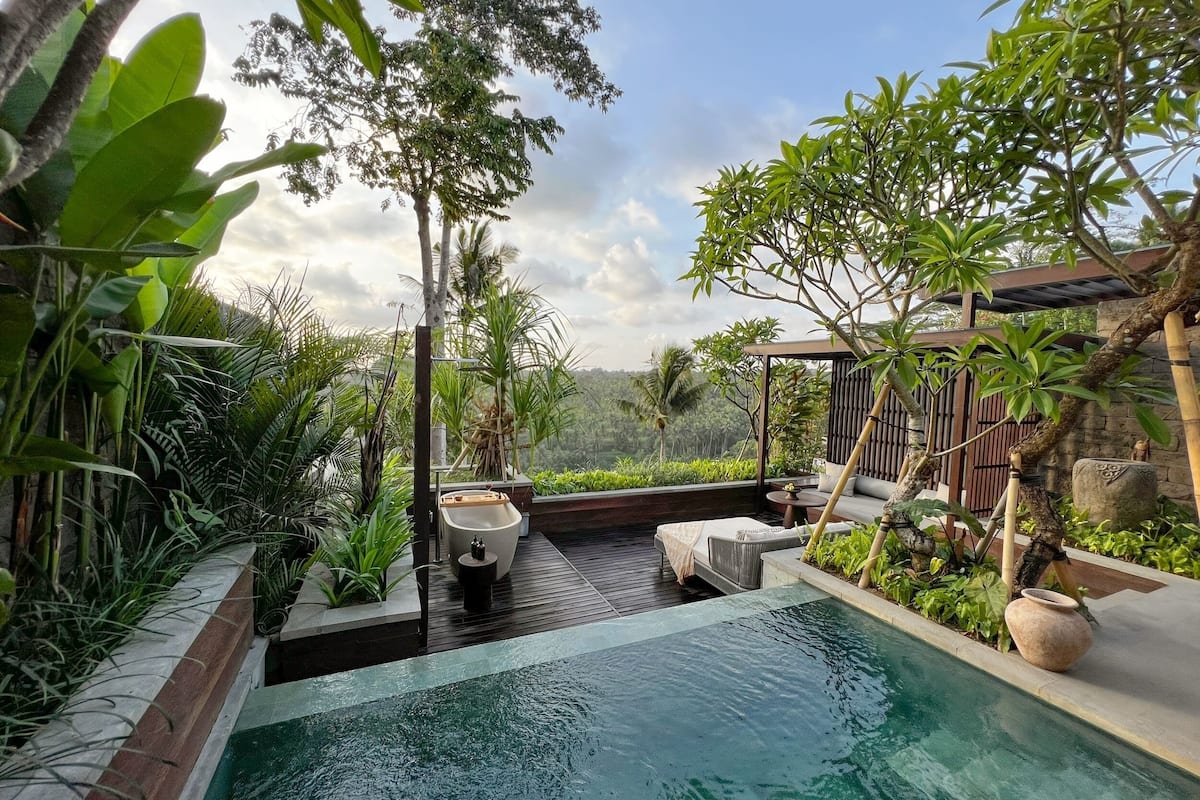 A serene outdoor pool area with a wooden deck, lounge chairs, and a small table.