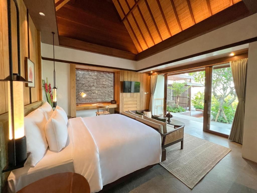 A hotel room with a large bed, a flat-screen TV, a dining table, and a sliding glass door leading to an outdoor area.