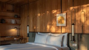 A bedroom with a wooden headboard, a bed with white linens, a nightstand, a reading lamp, and a framed picture on the wall. - The Ridge Bali (Ubud)