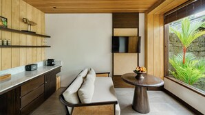 A modern kitchen with wooden cabinetry, a built-in bench, and a round table with a fruit bowl. - The Ridge Bali (Ubud)