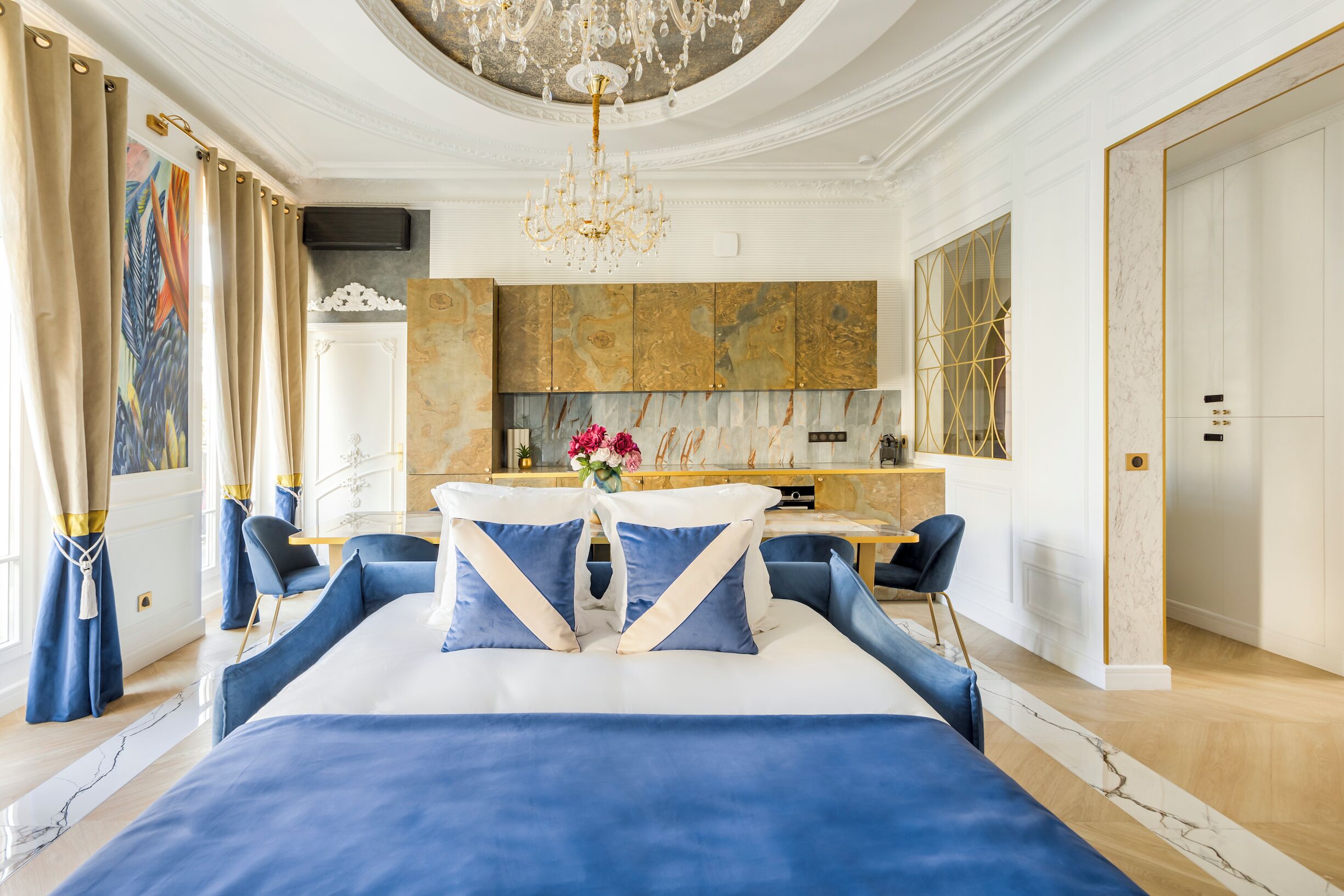 A luxurious bedroom with a large bed, a chandelier, and a modern kitchen in the background.