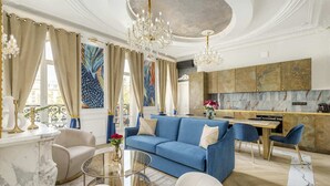 Una sala de estar amplia con un sofá azul, una chimenea de mármol y un comedor, con una cocina al fondo.