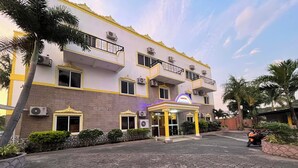A hotel with a central entrance, multiple balconies, and air conditioning units.