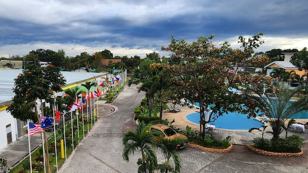A paved walkway lined with flags, a pool area, and palm trees.