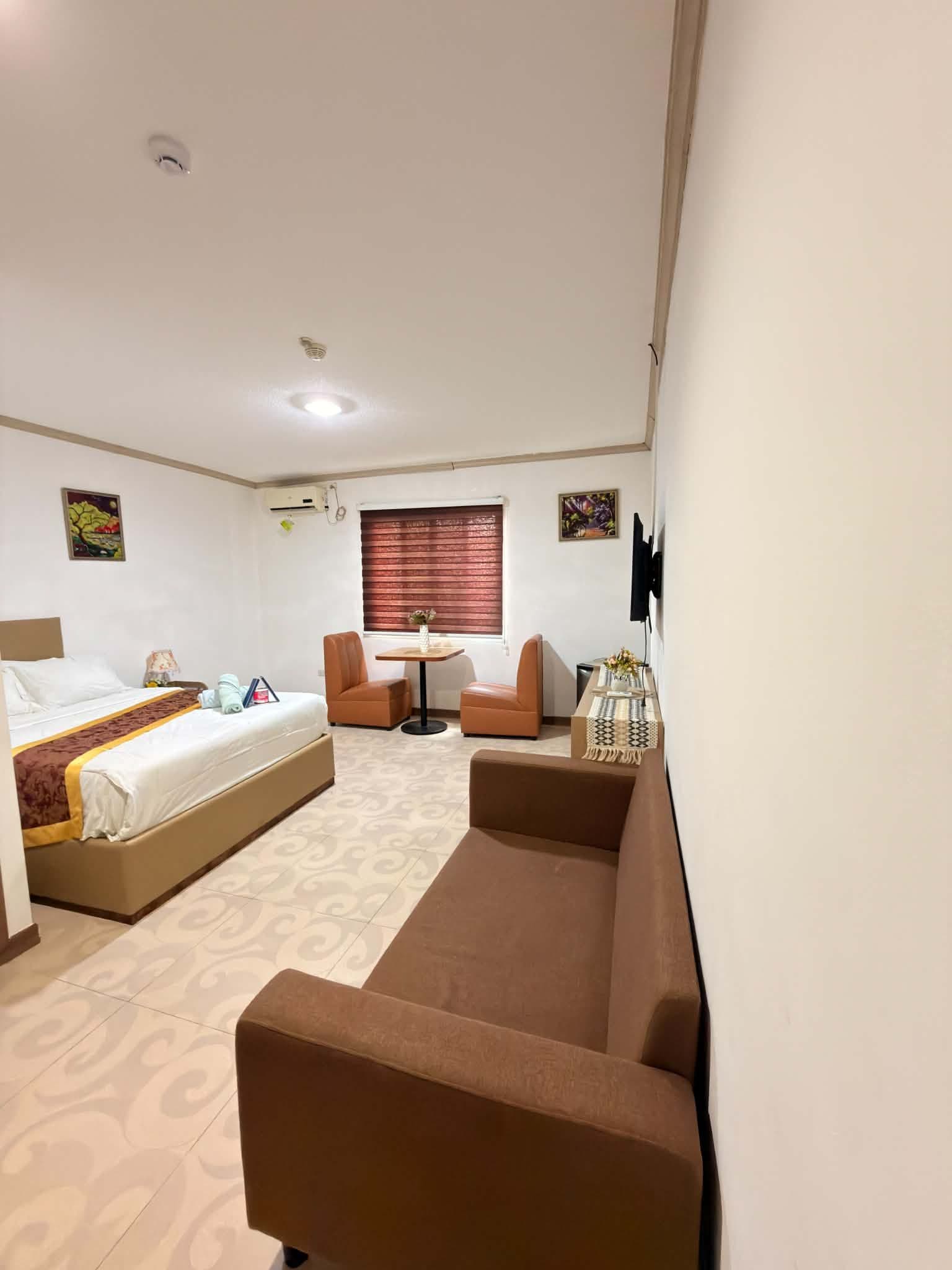 A hotel room with a bed, a sofa, a small table, and a TV mounted on the wall.