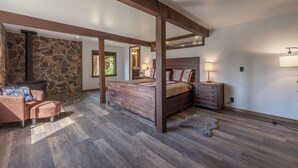 Ein Schlafzimmer mit Steinwand, Holzbalken, einem Bett, einem Nachttisch, einer Lampe und einem Sessel.