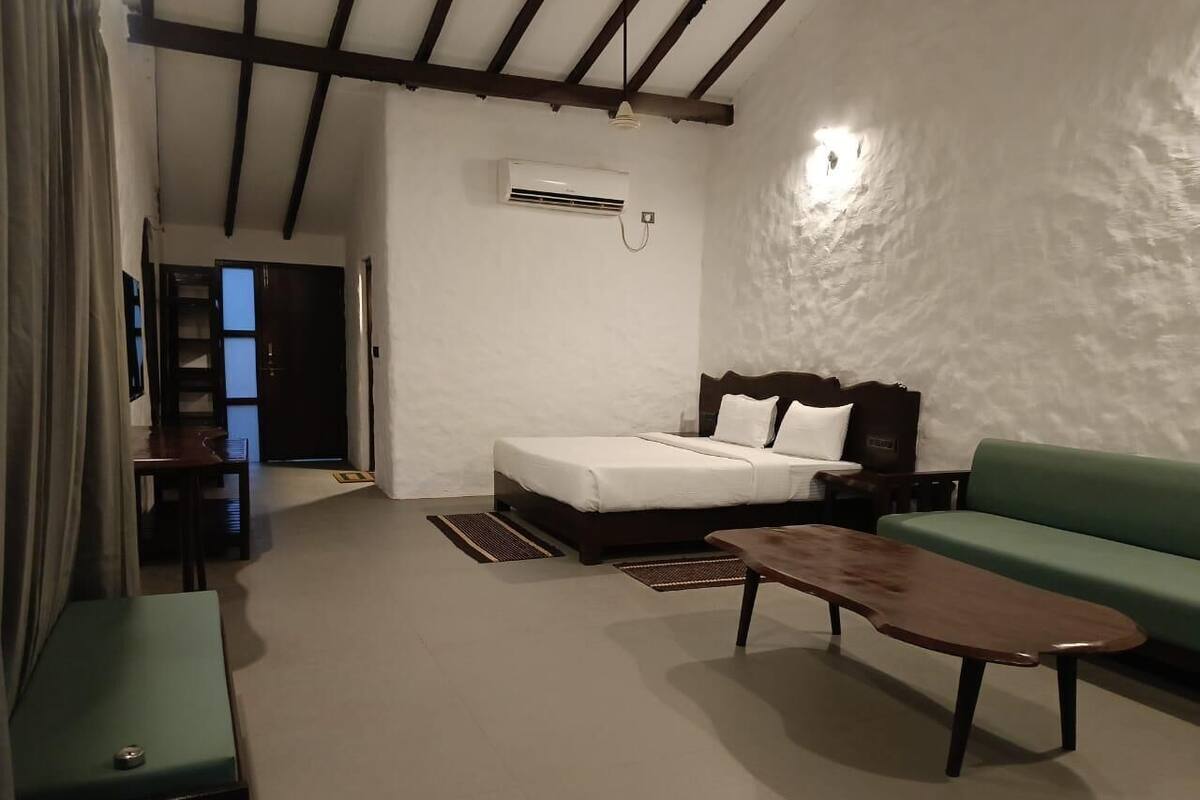 Habitación de hotel con cama, sofá verde, mesa de centro de madera, escritorio y equipo de aire acondicionado en la pared.
