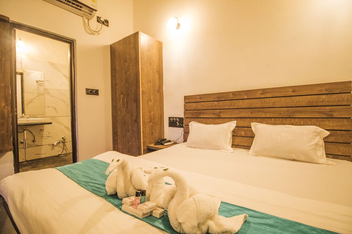 Una habitación de hotel con cabecera de madera, cama con ropa blanca y baño con ducha de mármol.