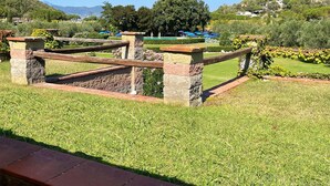 Un jardin bien entretenu, agrémenté d’une clôture en pierre, d’un espace piscine avec des parasols et offrant une vue sur un paysage vallonné.