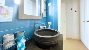 Une salle de bain avec des carreaux bleus, un grand lavabo, un miroir, un porte-serviettes et une poubelle.