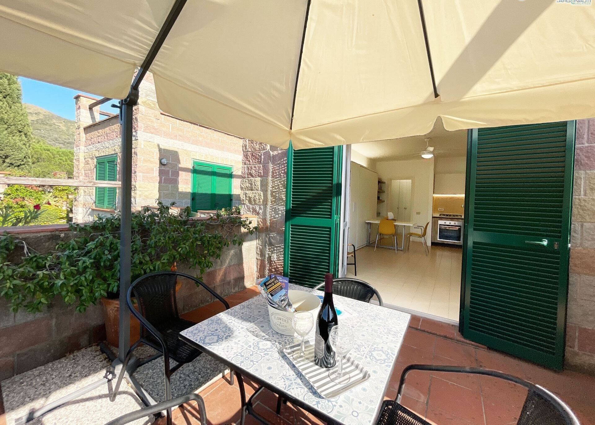 An outdoor patio with a table set for two, a bottle, and glasses.